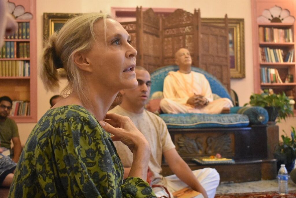 A woman speaks, with murti of Srila Prabhupada in the background.